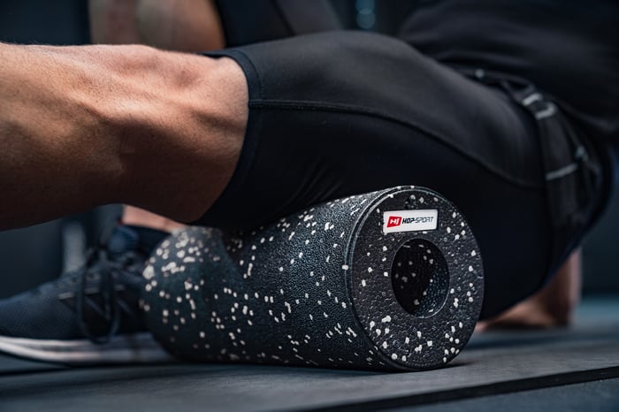 Uomo che massaggia i muscoli delle gambe con un rullo EPP 33cm bianco e nero del marchio Hop-Sport