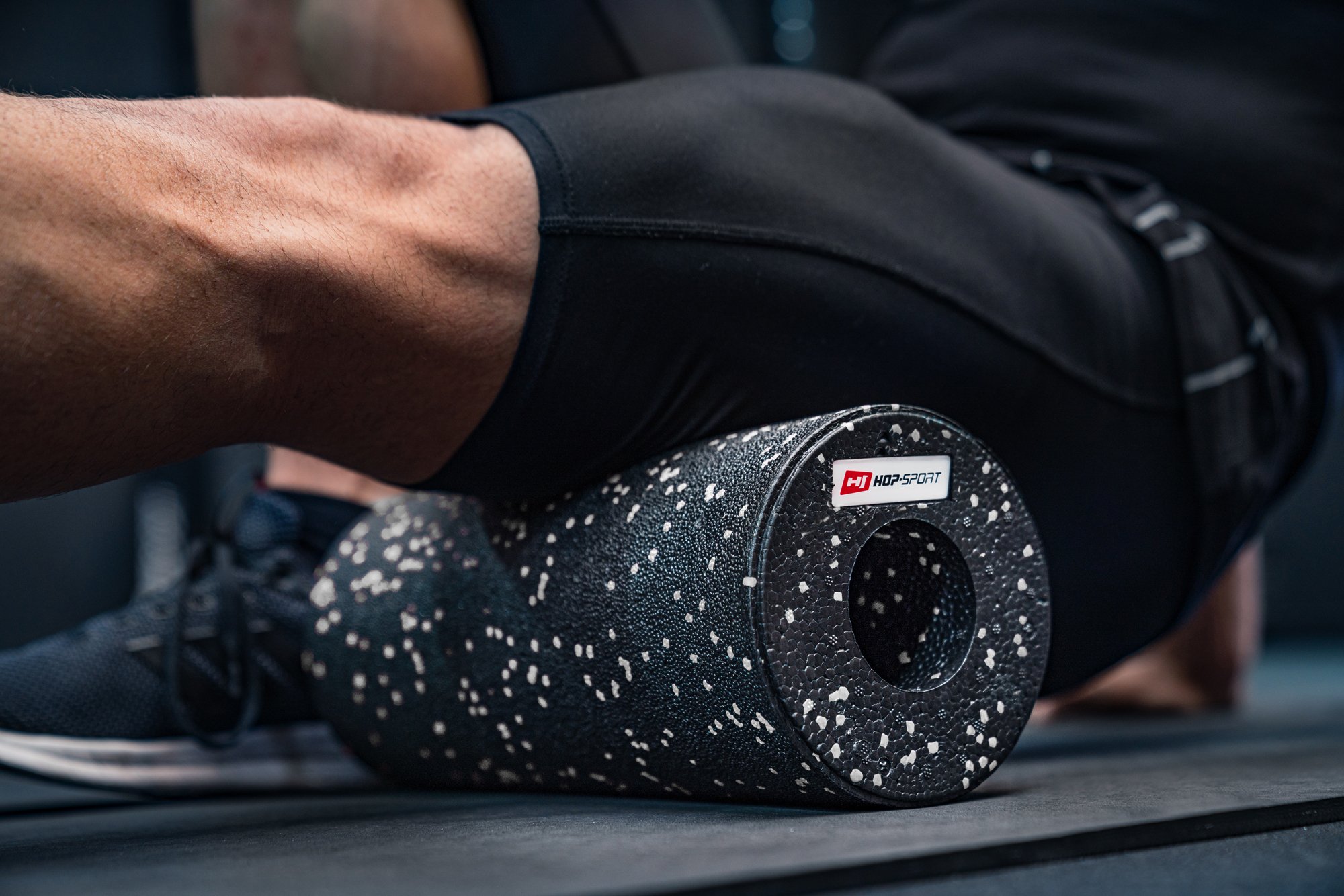 Uomo che massaggia i muscoli delle gambe con un rullo EPP 33cm bianco e nero del marchio Hop-Sport