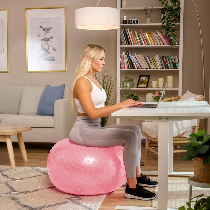 Donna usa la palla ginnica rosa con rilievi per lavorare alla scrivania